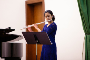 A girl in blue dress playing the flute.