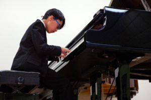 A young man playing the piano in front of an audience.