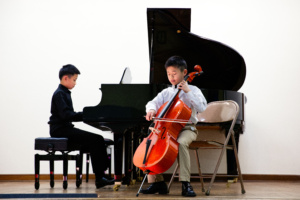 Two young boys playing musical instruments in a room.