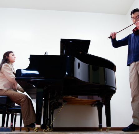 A man and woman playing musical instruments in front of a piano.