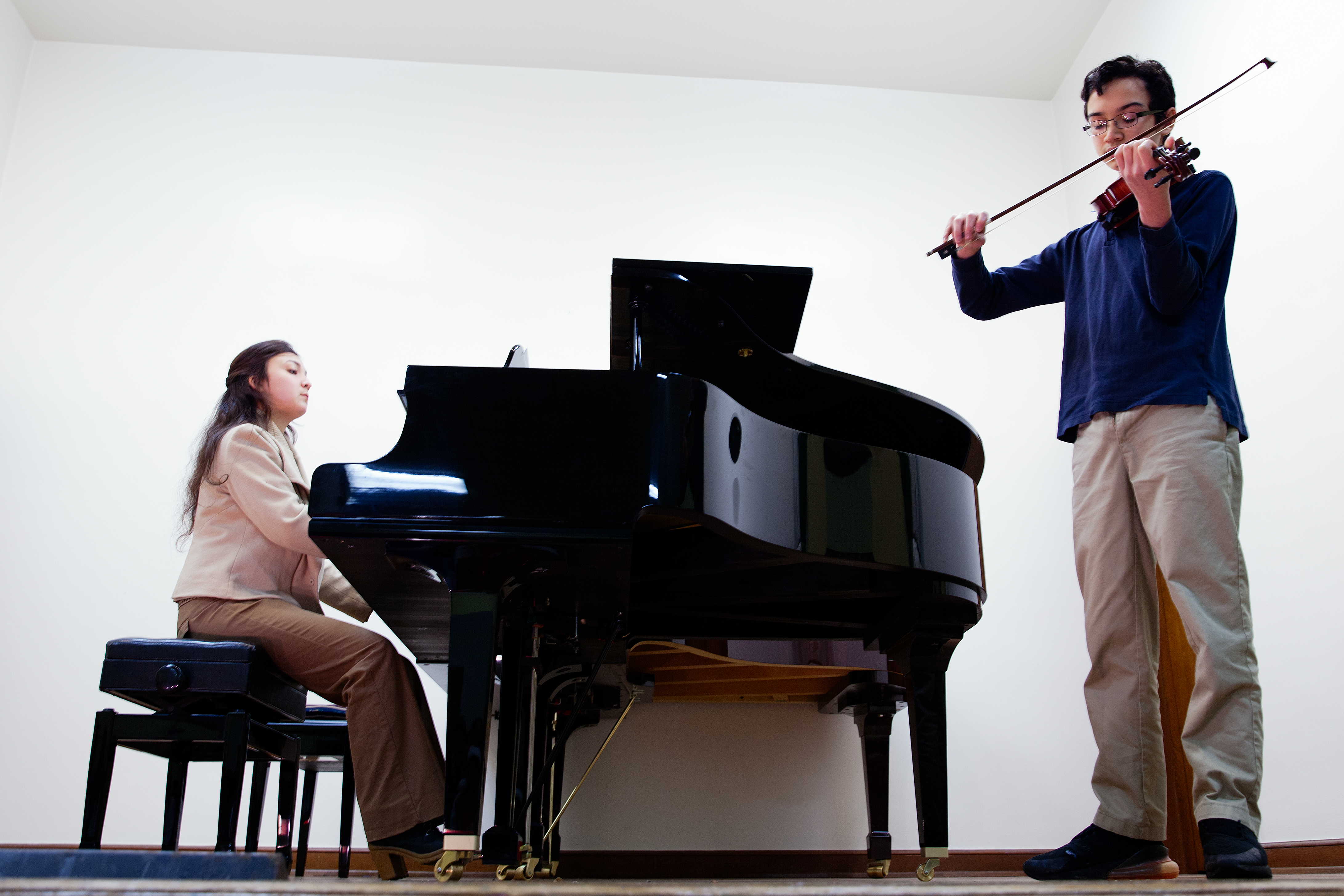 A man and woman playing musical instruments in front of a piano.