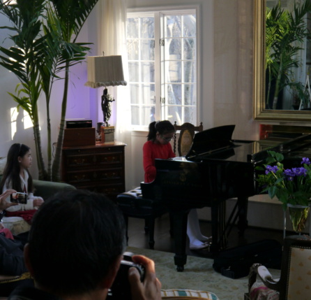 A group of people sitting around a living room playing piano.