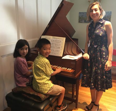 A woman and two children are playing the piano.