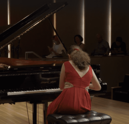 A woman in red dress playing piano with people sitting around.