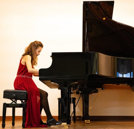 A woman in red dress playing piano on stool.