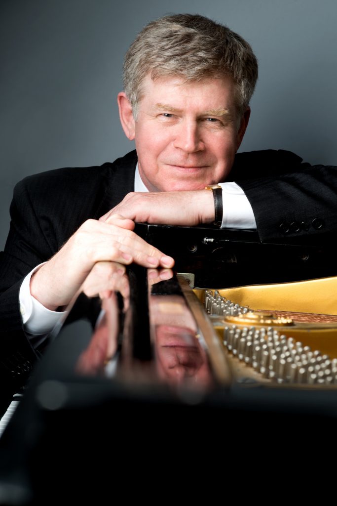 A man in suit and tie sitting at a piano.