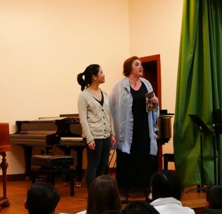 Two women sing in front of a group.