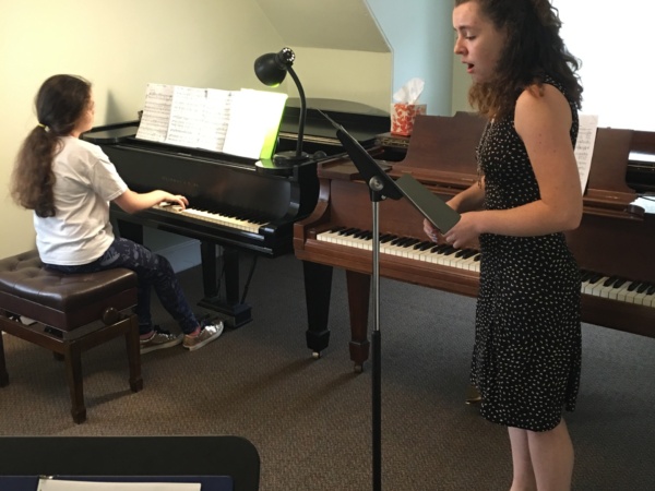 Two girls are practicing piano music in a room.