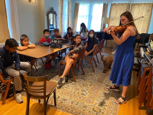 A woman playing the violin in front of a group of children.